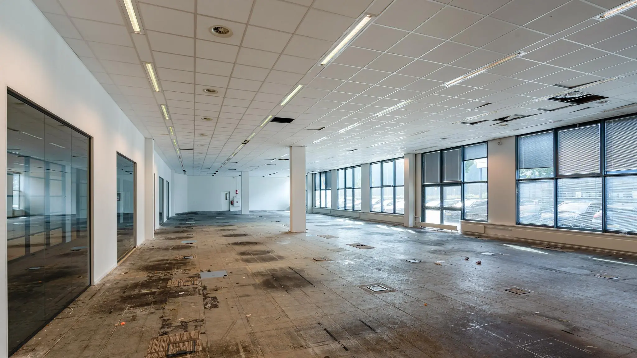 Leegstaand kantoorpand aan de Rivium Boulevard met grote ramen en een gestripte vloer.